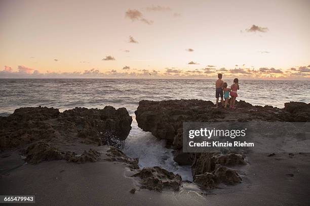 boy and sisters looking out from rocks at sunrise, blowing rocks preserve, jupiter island, florida, usa - blowing rocks preserve stock pictures, royalty-free photos & images