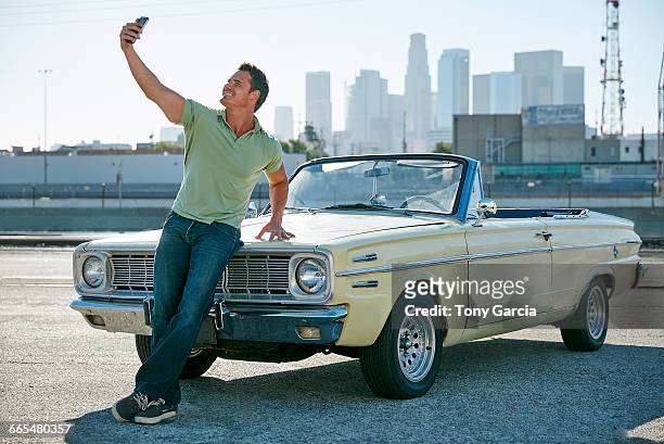 man leaning against convertible car taking selfie, los angeles, california, usa - selbstverliebt stock-fotos und bilder