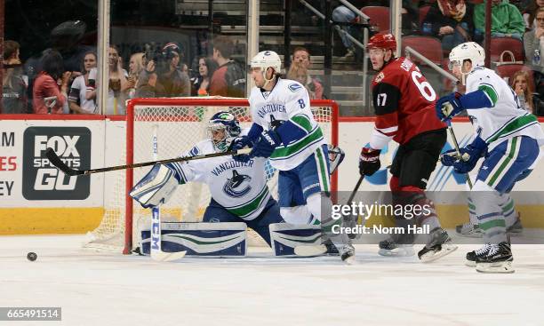 Goalie Ryan Miller of the Vancouver Canucks deflects the puck wide of the net and away from Lawson Crouse of the Arizona Coyotes as Christopher Tanev...