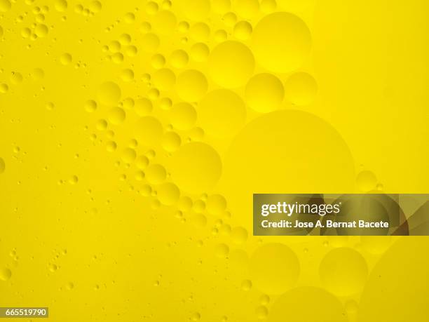 full frame of the textures formed by the bubbles and drops of oil in the shape of circle floating on a yellow colors background - burbuja stock pictures, royalty-free photos & images