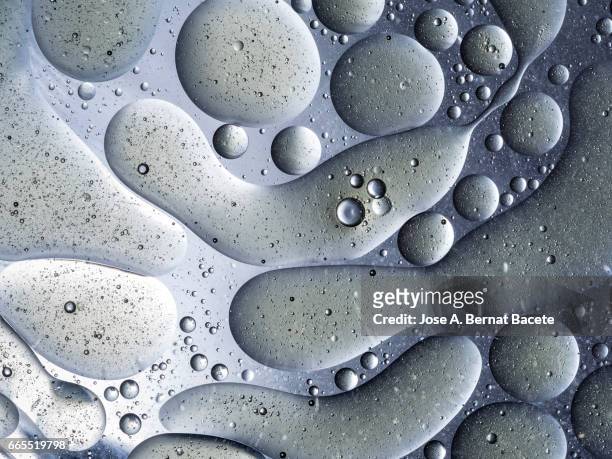 full frame of the textures formed by the bubbles and drops of oil in the shape of circle floating on a gray and yellow colors background - simetría stockfoto's en -beelden