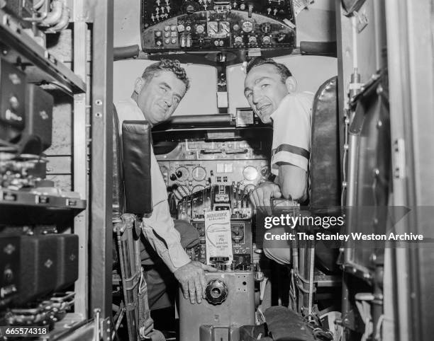 Carmen Basilio sitting with the pilot in the cockpit of a Mohawk Airlines airplane in Watertown, New York, August 20, 1957.