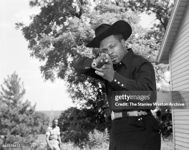 Archie Moore dressed as a cowboy aims his rifle at the camera at this training camp in North Adams, Massachusetts, circa 1955.