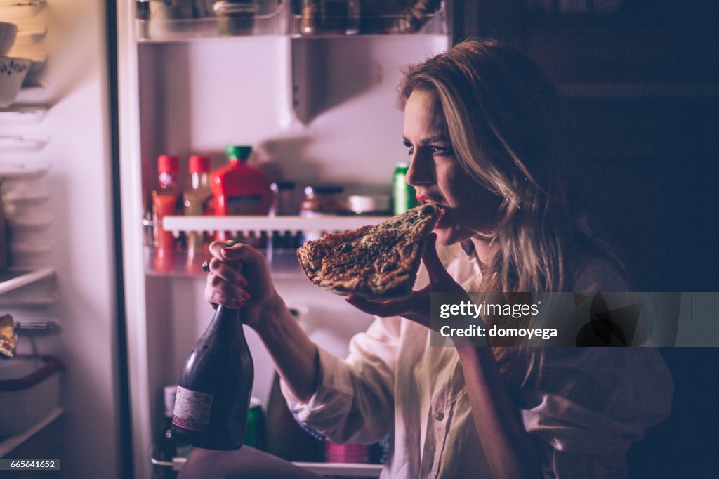 ピザを食べて、夜の間に冷蔵庫の前でワインを飲む女