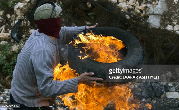 Palestinian protestor carries a burning car tire during clashes with Israeli security forces following a weekly demonstration against the...