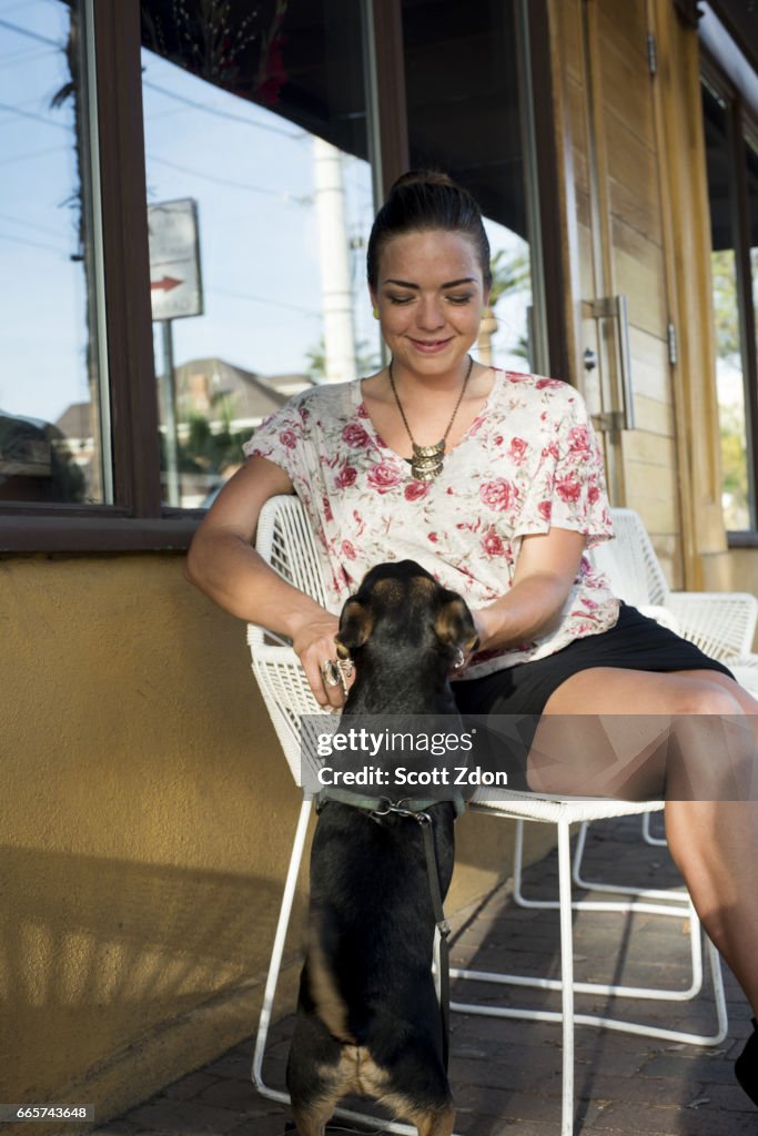 Caucasian woman sitting with dog at neighborhood cafe.