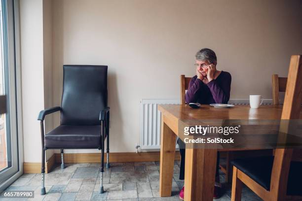 senior mujer sentada al lado de una silla vacía - viuda fotografías e imágenes de stock