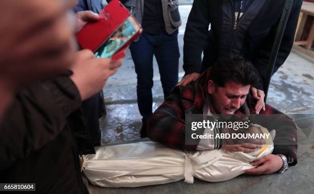 The father of one-year-old infant Amira grieves over her body as others wrap the burial shrowd in a make-shift morgue, after she died in a reported...