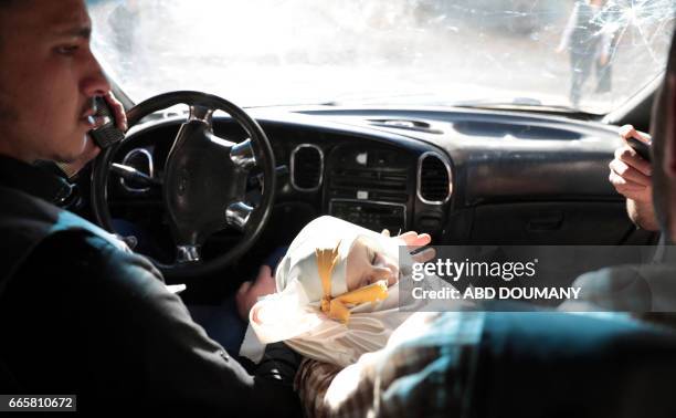 Syrian holds the body of one-year-old infant Amira as it lies wrapped in its shrowd en route to her burial in a vehicle, after she died in a reported...