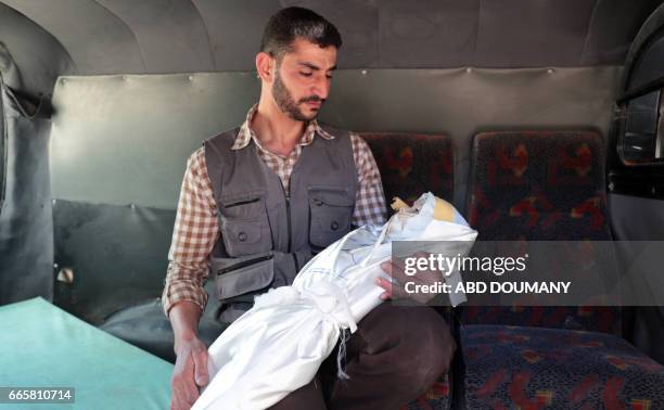 Syrian holds the body of one-year-old infant Amira as it lies wrapped in its shrowd en route to her burial in a vehicle, after she died in a reported...