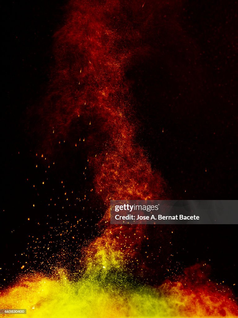 Explosion of a cloud of powder of particles of  colors yellow and orange on a black background
