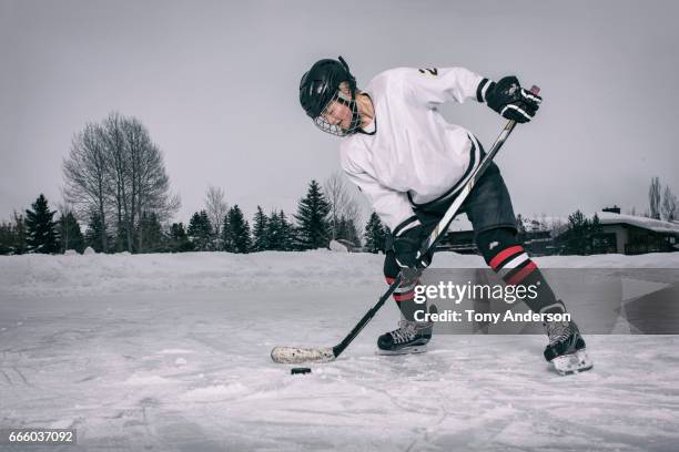 teenage girl ice hockey player taking a shot on outdoor rink in winter - centro hóquei no gelo - fotografias e filmes do acervo