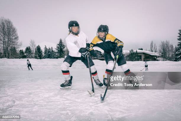 one teenage girl hockey player body checking another on outdoor rink in winter - hockey helmet stock pictures, royalty-free photos & images
