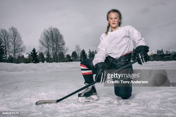 teenage girl ice hockey player kneeling on rink outdoors in winter - alleen één meisje stockfoto's en -beelden