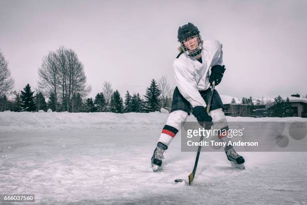 teenage girl ice hockey player taking a shot on outdoor rink in winter - hockey helmet stock pictures, royalty-free photos & images