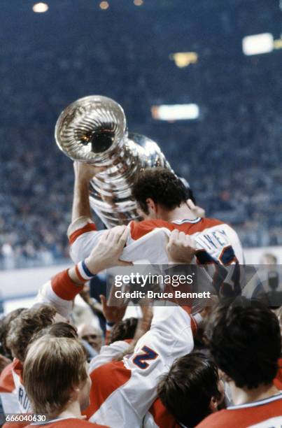 Bob Gainey of the Montreal Canadiens is held aloft by his teammates as he holds up the Stanley Cup Trophy after his team defeated the New York...