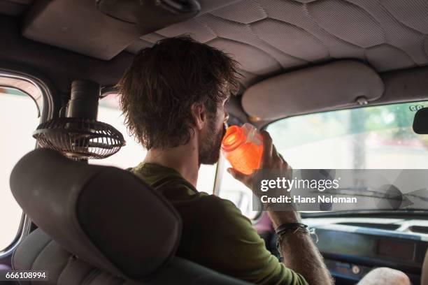 man drinking water inside a car - vista trasera de tres cuartos fotografías e imágenes de stock