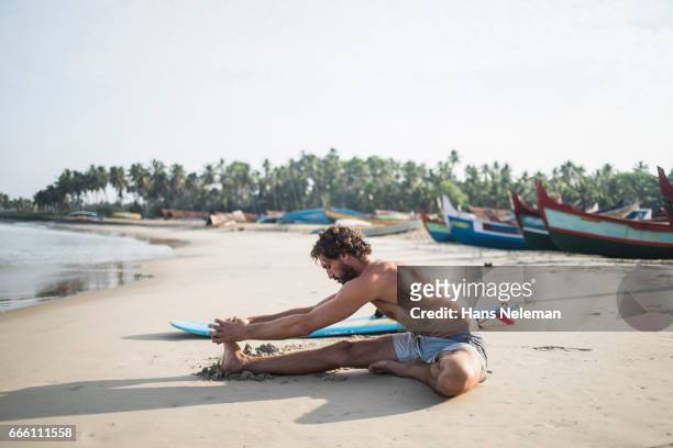 male surfer stretching on the beach - kerala surf stock-fotos und bilder