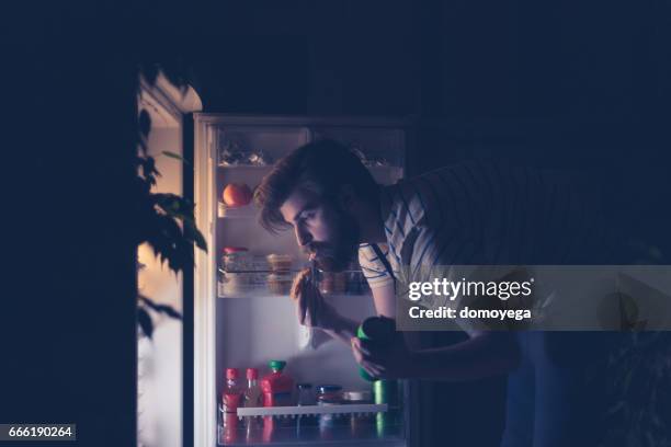 uomo che beve snack e beve birra a tarda notte davanti al frigorifero - rimpinzarsi foto e immagini stock