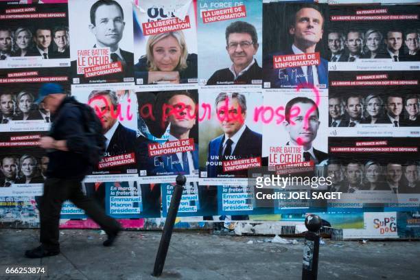 Man passes in front of a wall of election campaign posters of different candidates, French presidential election candidate for the left-wing French...