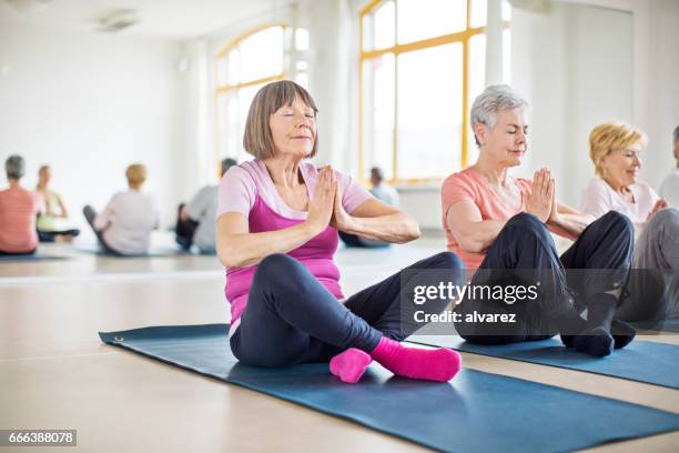 senior women meditating in yoga class - senior women yoga stock pictures, royalty-free photos & images