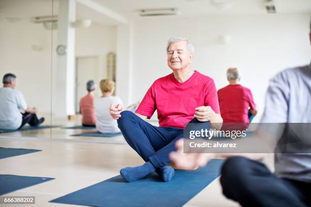 entspannte senior woman meditieren im yoga-kurs - senior yoga stock-fotos und bilder