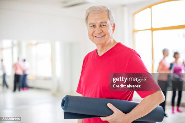 sonriente a hombre senior con estera del ejercicio en clase - un solo hombre mayor fotografías e imágenes de stock