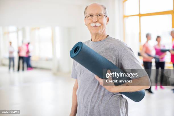 senior man holding exercise mat in yoga class - bigode imagens e fotografias de stock