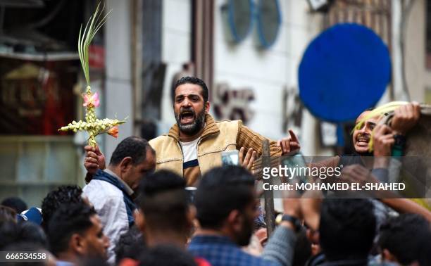 An Egyptian raises a cross made of palm leaves, originally intended for Palm Sunday celebrations, as he is being lifted by others gathering outside...