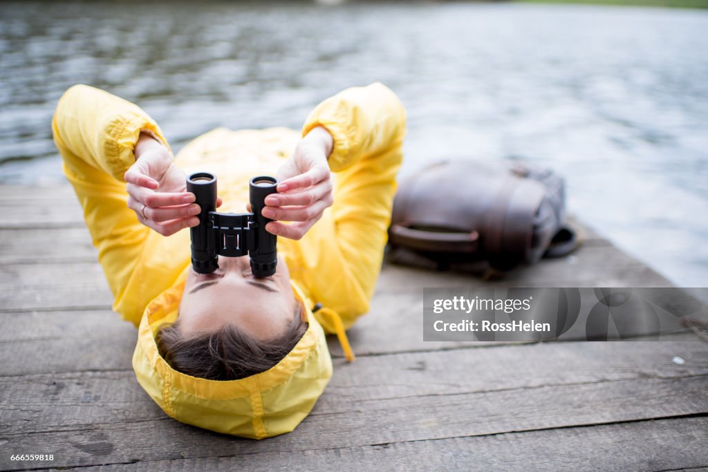 Woman in yellow raincoat lying with binoculars outdoors