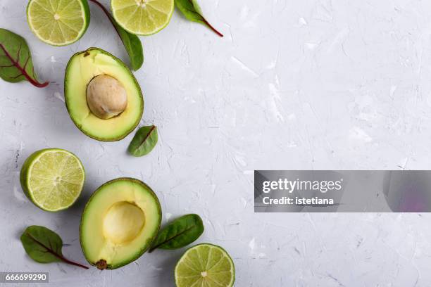 food background with fresh organic avocado and lime over light gray plaster texture table - mexican food background stock pictures, royalty-free photos & images