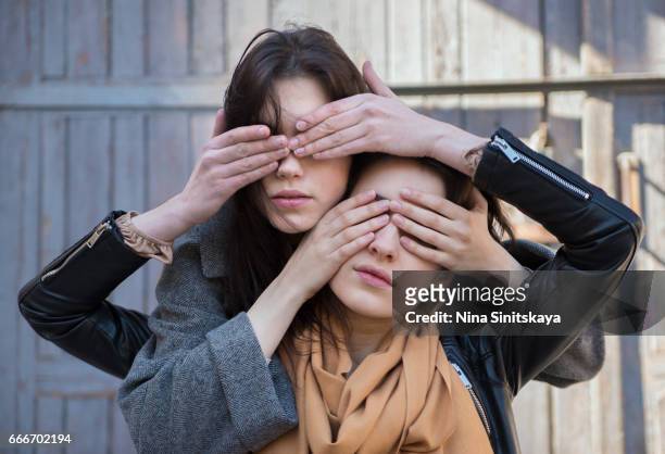 two females closing each others eyes, outdoor - truth lies foto e immagini stock