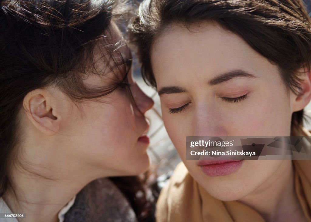 A girl whispering to the ear of another girl, outdoor