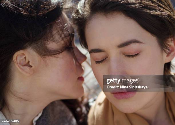 a girl whispering to the ear of another girl, outdoor - whispering stock pictures, royalty-free photos & images