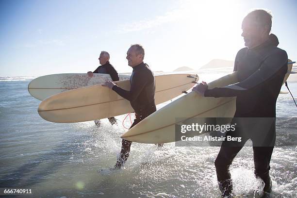 senior surfers on a beach at sunset - wetsuit stock pictures, royalty-free photos & images