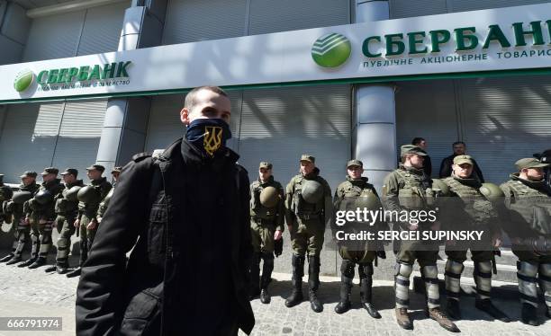 An activist walks in front of Ukrainian National Guard soldiers guarding the Russian owned Sberbank Bank in Kiev on April 10, 2017. Ukrainian...