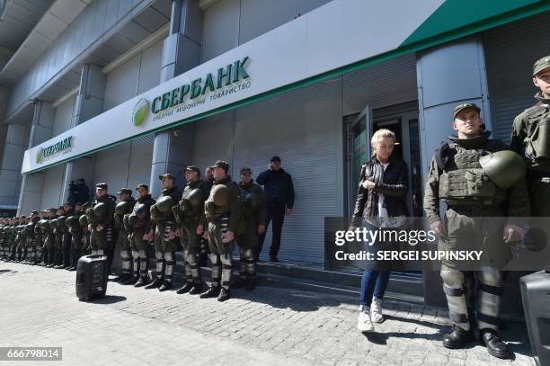 Client leaves the Russian owned Sberbank Bank walking past past Ukrainian National Guard soldiers guarding the Russian owned Bank from protesting...