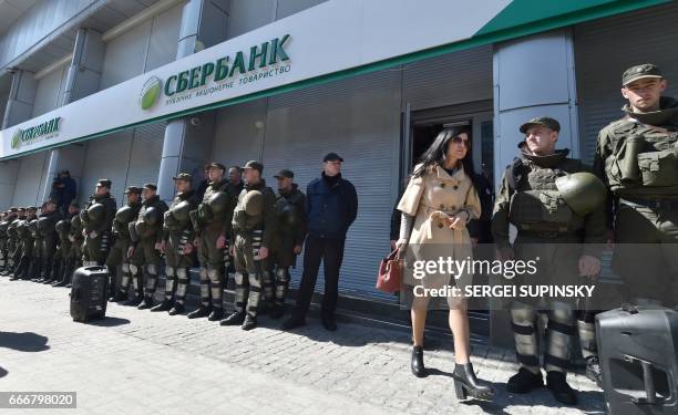 Client leaves the Russian owned Sberbank Bank walking past past Ukrainian National Guard soldiers guarding the Russian owned Bank from protesting...