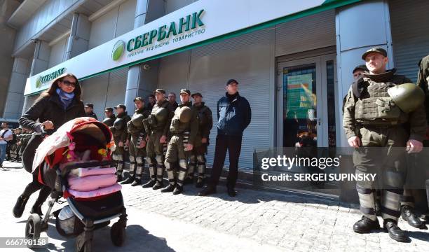 Woman pushes a pram past Ukrainian National Guard soldiers guarding the Russian owned Sberbank Bank from protesting activists in Kiev on April 10,...