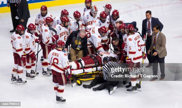 Tariq Hammond of the Denver Pioneers is greeted by his teammates as he is taken off the ice on a stretcher after he crashed into the boards breaking...