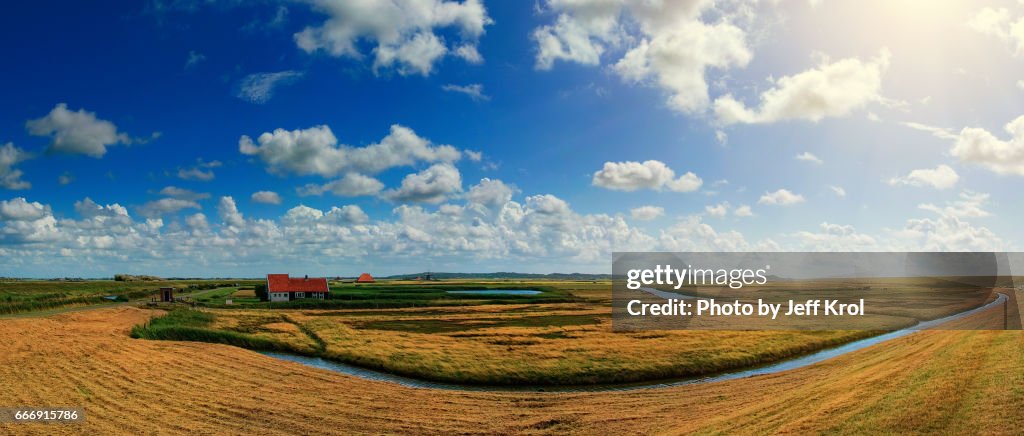 Panoramic dutch landscape view of nature, blue cloudy sky with sun in the back.