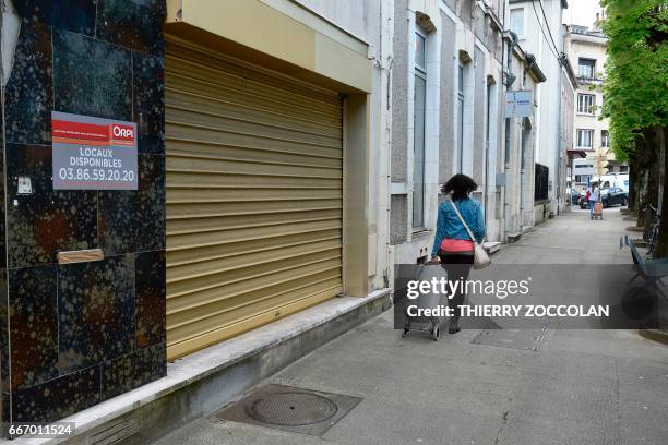 Woman walks past a closed business in Nevers, central France, on April 4, 2017. The population of the picturesque town on the Loire river has fallen...