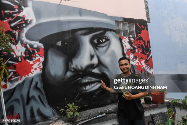 This picture taken on February 20, 2017 shows An, a graffiti artist and vendor of spray cans, posing in front of a portrait of US rapper Ice Cube at...