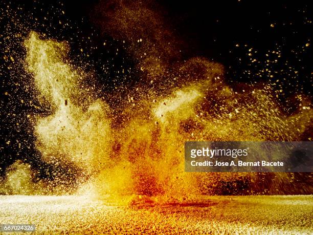 explosion of a cloud of powder of particles of orange and yellow color on a black background - ground culinary - fotografias e filmes do acervo