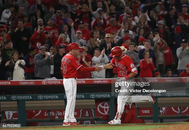 Mike Trout of the Los Angeles Angels of Anaheim gets a handshake from third base coach Ron Roenicke after Trout hit a two-run homerun during the...