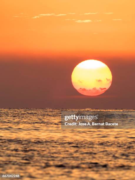 full frame of a sunset sun with high clouds of colors orange, next to sea water - cielo dramático stock-fotos und bilder