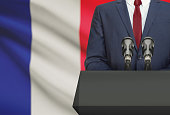 Businessman or politician making speech from behind a pulpit with national flag on background - France