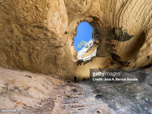 persons inside a great cave eroded with a hole in the ceiling by which the sky is seen - agujero stockfoto's en -beelden