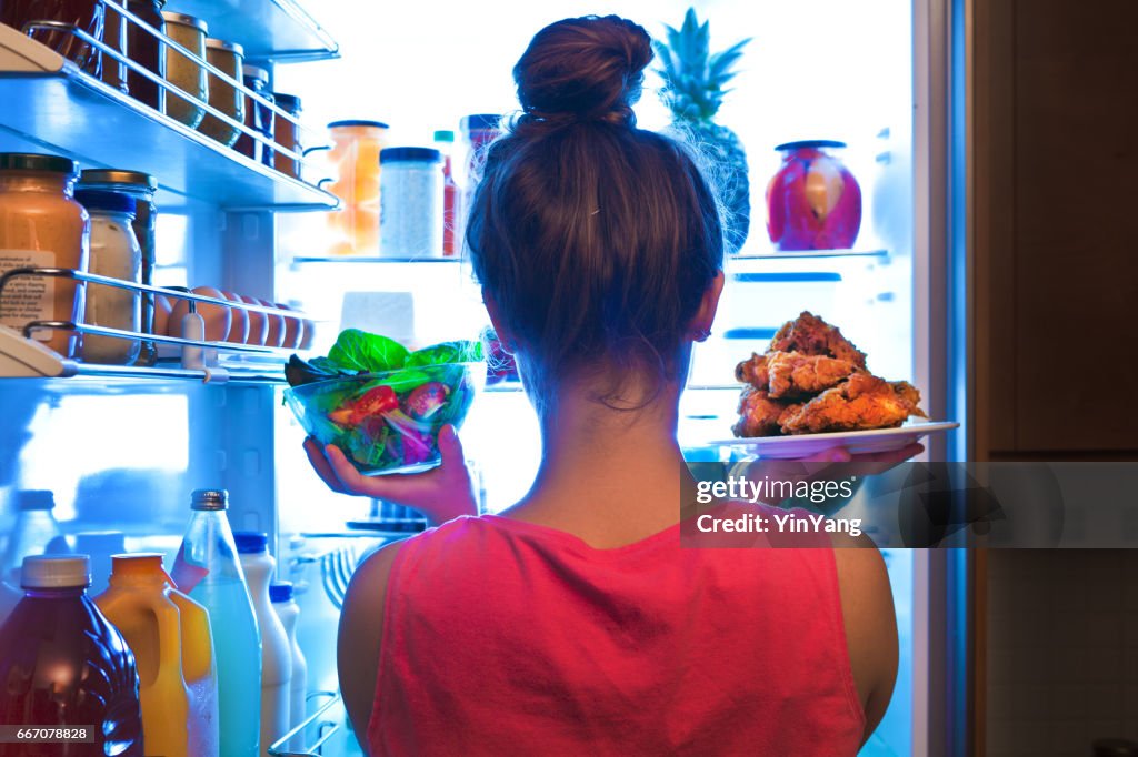 Jonge vrouw maken van keuzes voor een gezonde salade of Junk Food gebakken kip