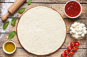 Raw dough for pizza with ingredient: tomato sauce, dough, mozzarella, tomatoes, basil, olive oil, spices served on rustic wooden table. Aerial shot, copyspace for text.